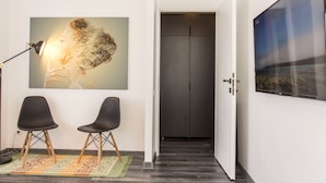 A hallway with a modern interior, featuring a large abstract painting, two black chairs, a patterned rug, and a door leading to a room with a large window. - Studio L by MRG Apartments (Bucharest)