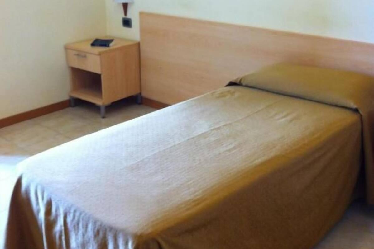 Una cama individual con cabecera de madera en una habitación con mesita de noche y lámpara.