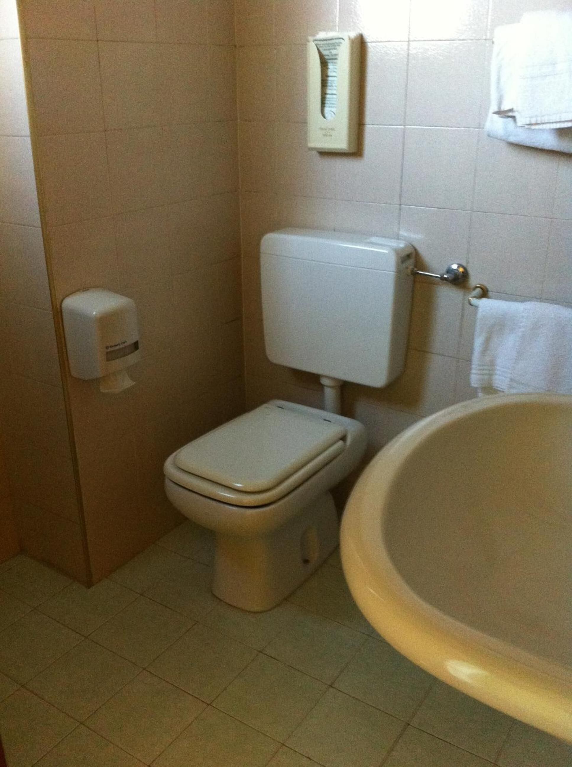 A small bathroom with a toilet, a hand soap dispenser, and a sink.