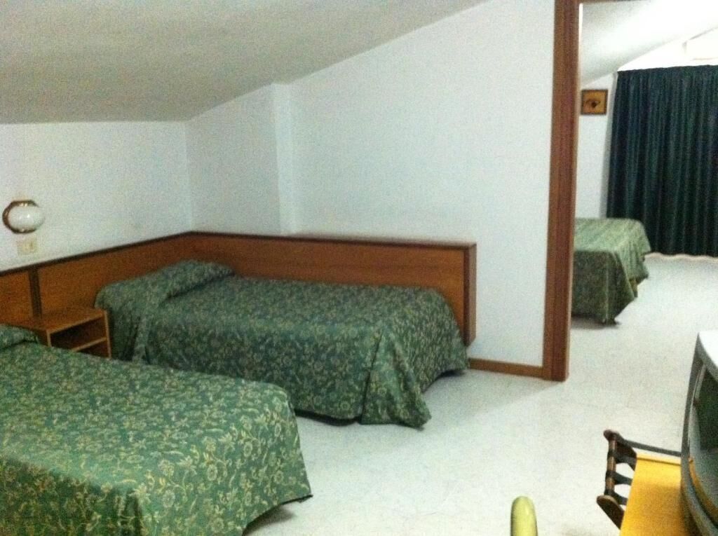 Una habitación con dos camas, un cabecero de madera, una mesita pequeña y un televisor.