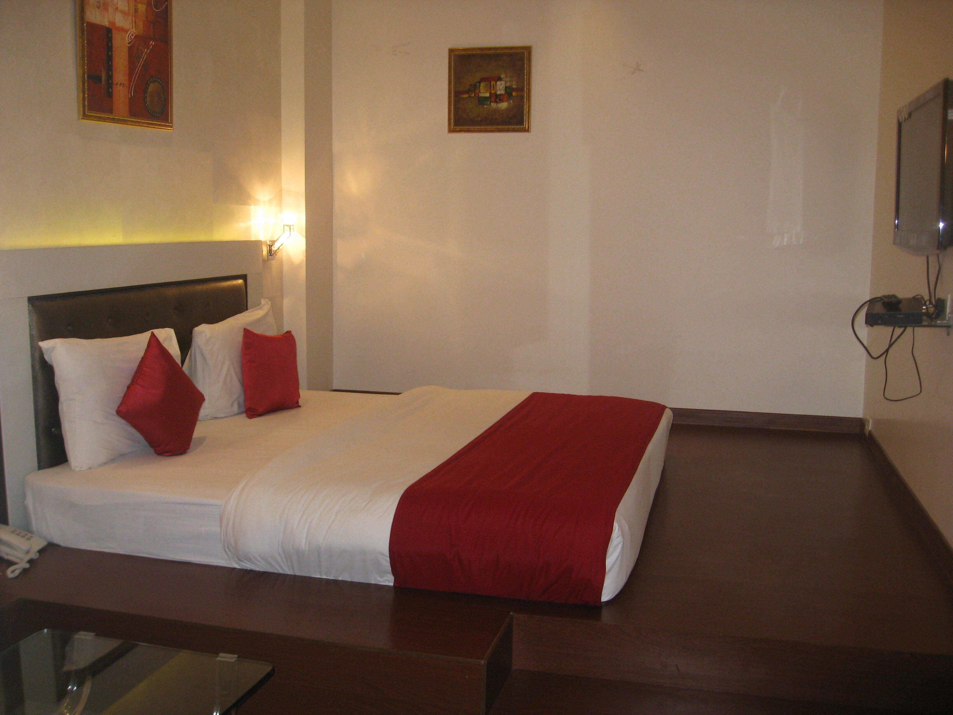 A hotel room with a bed, a bedside table, a wall-mounted TV, and a painting.