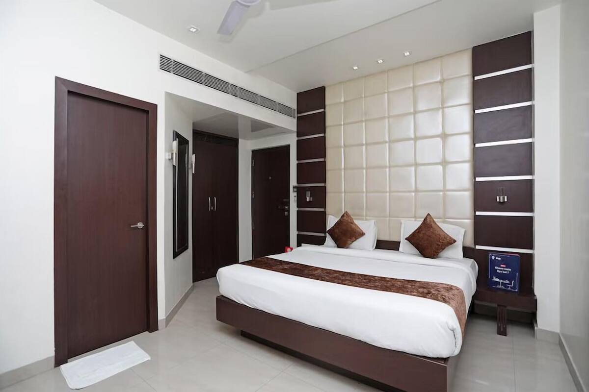 A modern hotel room with a large bed, dark wood wardrobe, and a wall-mounted panel design.