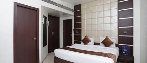 A modern hotel room with a large bed, dark wood wardrobe, and a wall-mounted panel design.