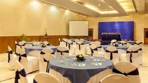 A conference room with round tables, white chairs with blue sashes, and a stage with a blue backdrop. - Hotel D Grand (Bareilly)