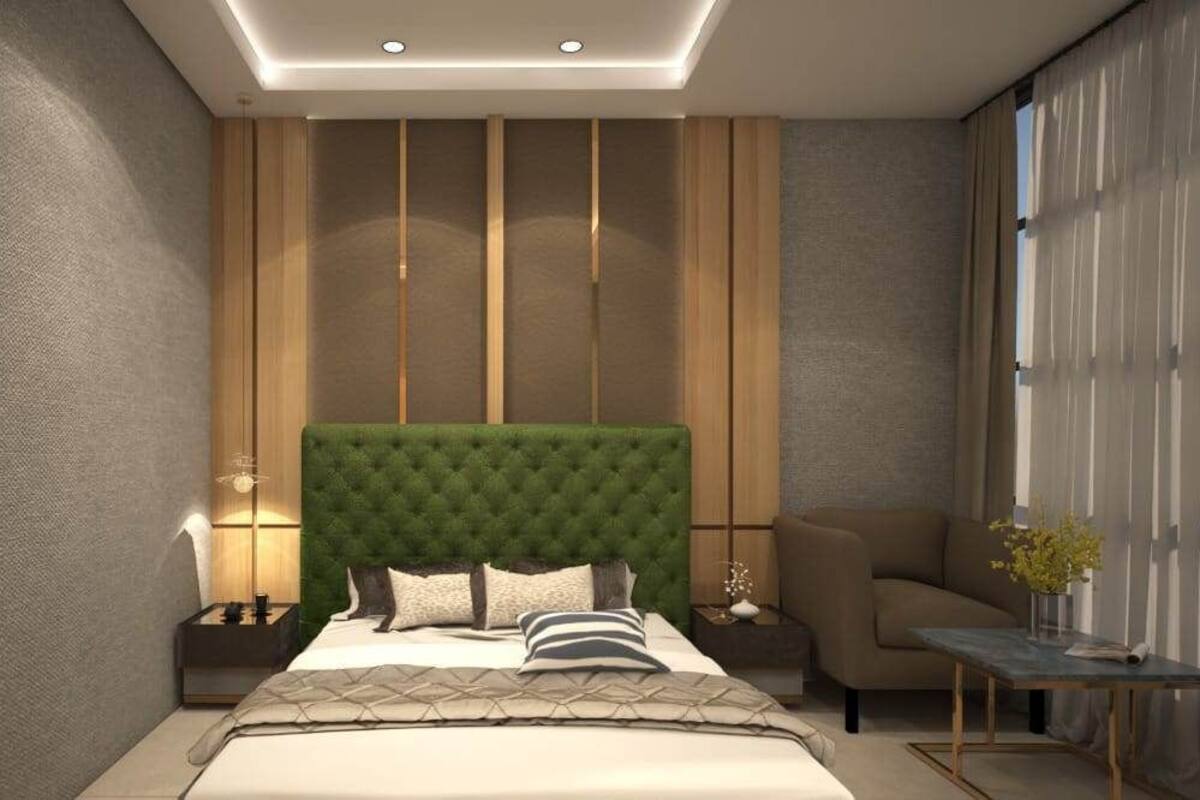 A modern bedroom with a tufted green headboard, a bed with multiple pillows, a nightstand with a lamp, a side table with a vase, and a chair.