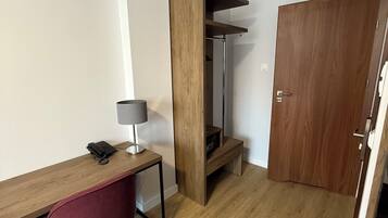 Una habitación pequeña y luminosa, con un escritorio de madera, una silla roja, un armario de madera y una puerta.