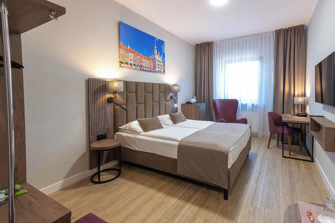 Una habitación de hotel con una cama grande, un escritorio con silla, un televisor y un cuadro de un paisaje urbano en la pared.