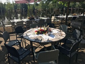 An outdoor dining area with round tables, wicker chairs, and floral centerpieces. - Hotel Buenos (Geldrop)