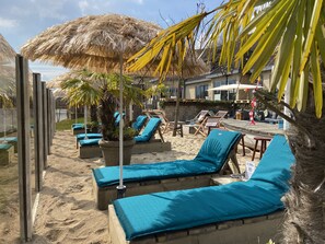 A beachside lounge area with sun loungers and a thatched umbrella. - Hotel Buenos (Geldrop)