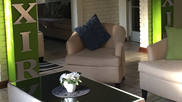 Ett vardagsrum med en beige soffa, ett svart soffbord med en vit vas och en grön accentvägg där ordet ”ELIXIR” är skrivet vertikalt.