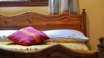 A wooden bed with a patterned bedspread and a single red and pink pillow.