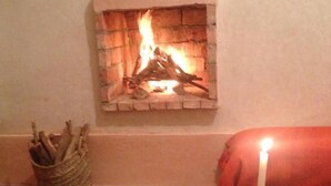 A cozy room with a fireplace, a woven basket, a patterned rug, and a candle on the floor. - Riad Diwane (Ouirgane)