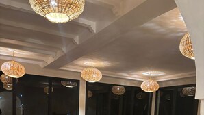 An indoor dining area with multiple tables and chairs, large windows, and hanging wicker lamps. - Riad Diwane (Ouirgane)