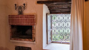 A rustic room with a brick fireplace, a window with decorative iron bars, and a wooden beam above the window. - Riad Diwane (Ouirgane)