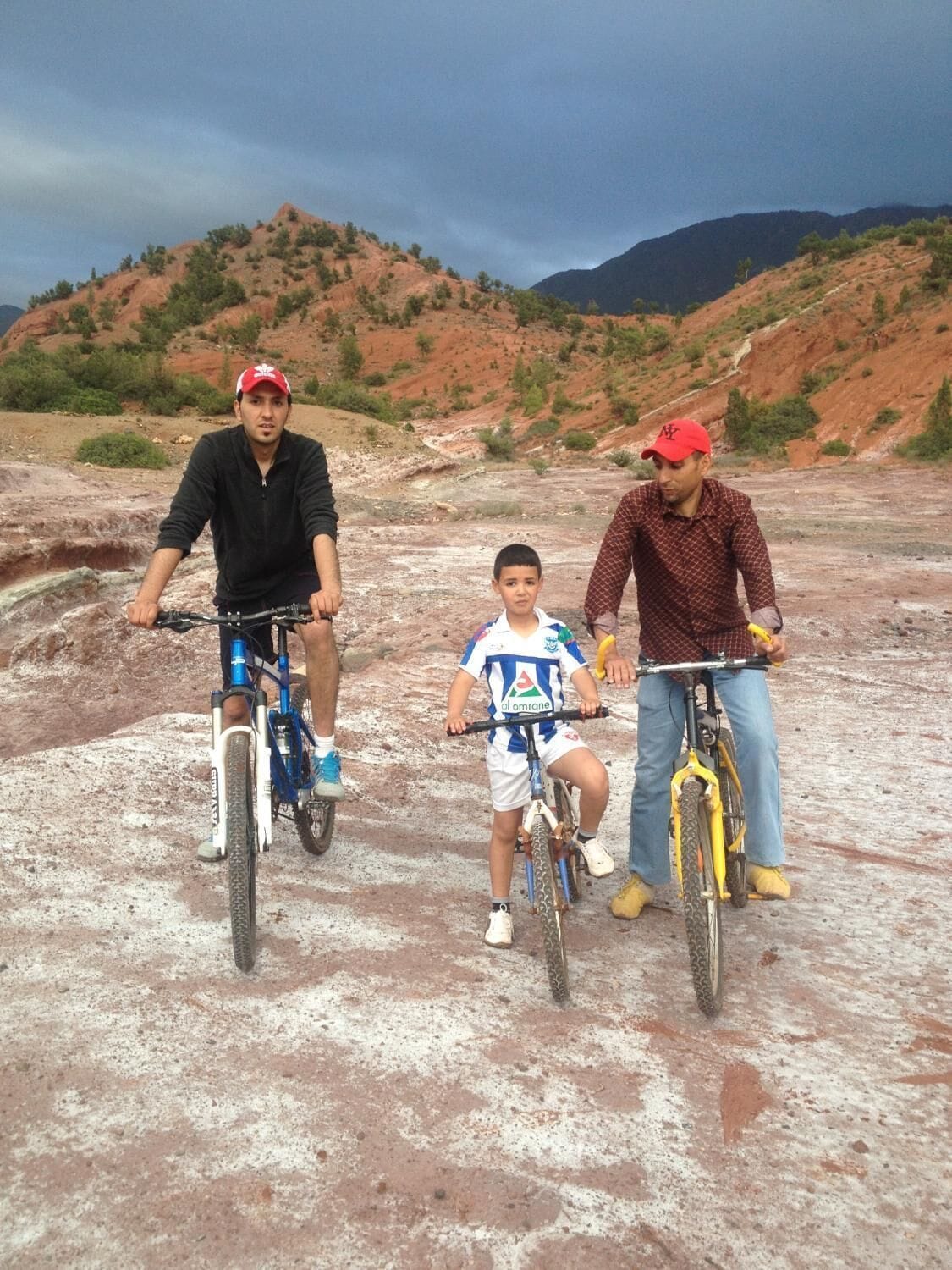 Tres personas en bicicletas en un entorno rocoso al aire libre, con colinas al fondo.