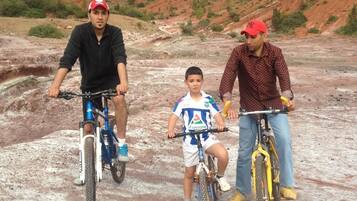 Tres personas en bicicletas en un entorno rocoso al aire libre, con colinas al fondo.