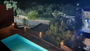A nighttime view of a swimming pool area with a view of a residential area in the background. - Riad Diwane (Ouirgane)