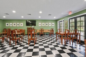 A dining area with checkered flooring, wooden tables and chairs, framed pictures on the walls, and a large window with a view. - Greenwood Plantation B&B (St. Francisville)
