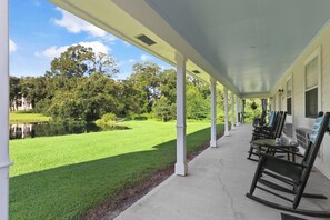 A covered porch with a view of a well-maintained lawn and a body of water. - Greenwood Plantation B&B (St. Francisville)