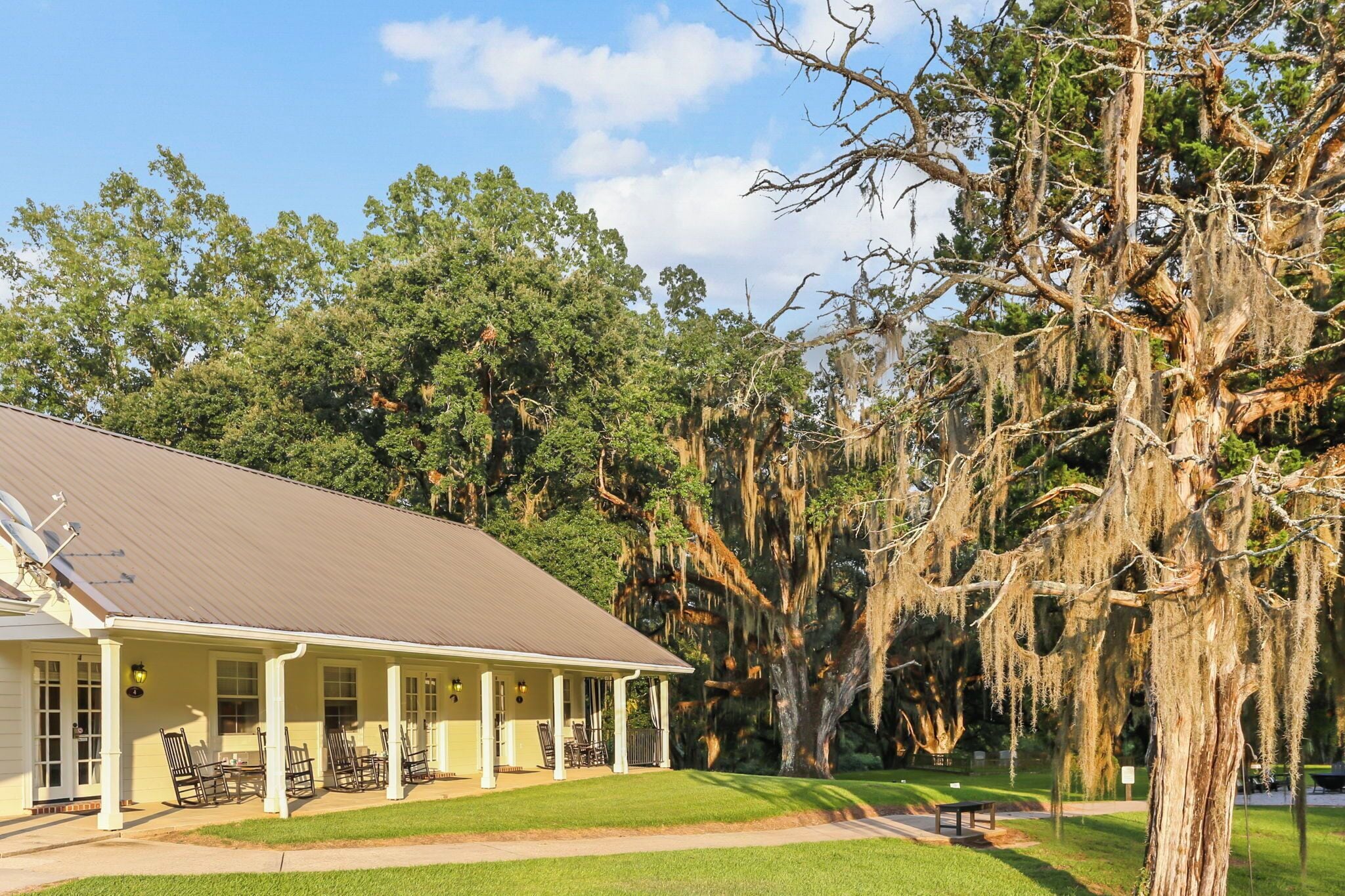 A two-story house with a porch, surrounded by lush greenery and trees with Spanish moss.