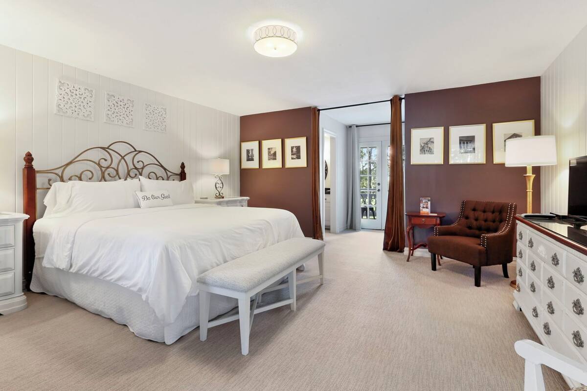 A hotel room with a large bed, a bench, a chair, a dresser, and framed pictures on the wall.
