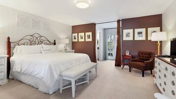 Une chambre d’hôtel avec un grand lit, un banc, une chaise, une commode et des tableaux encadrés au mur.