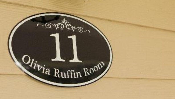 A circular sign with the number 11 and the text "Olivia Ruffin Room" on a wooden surface. - Greenwood Plantation B&B (St. Francisville)