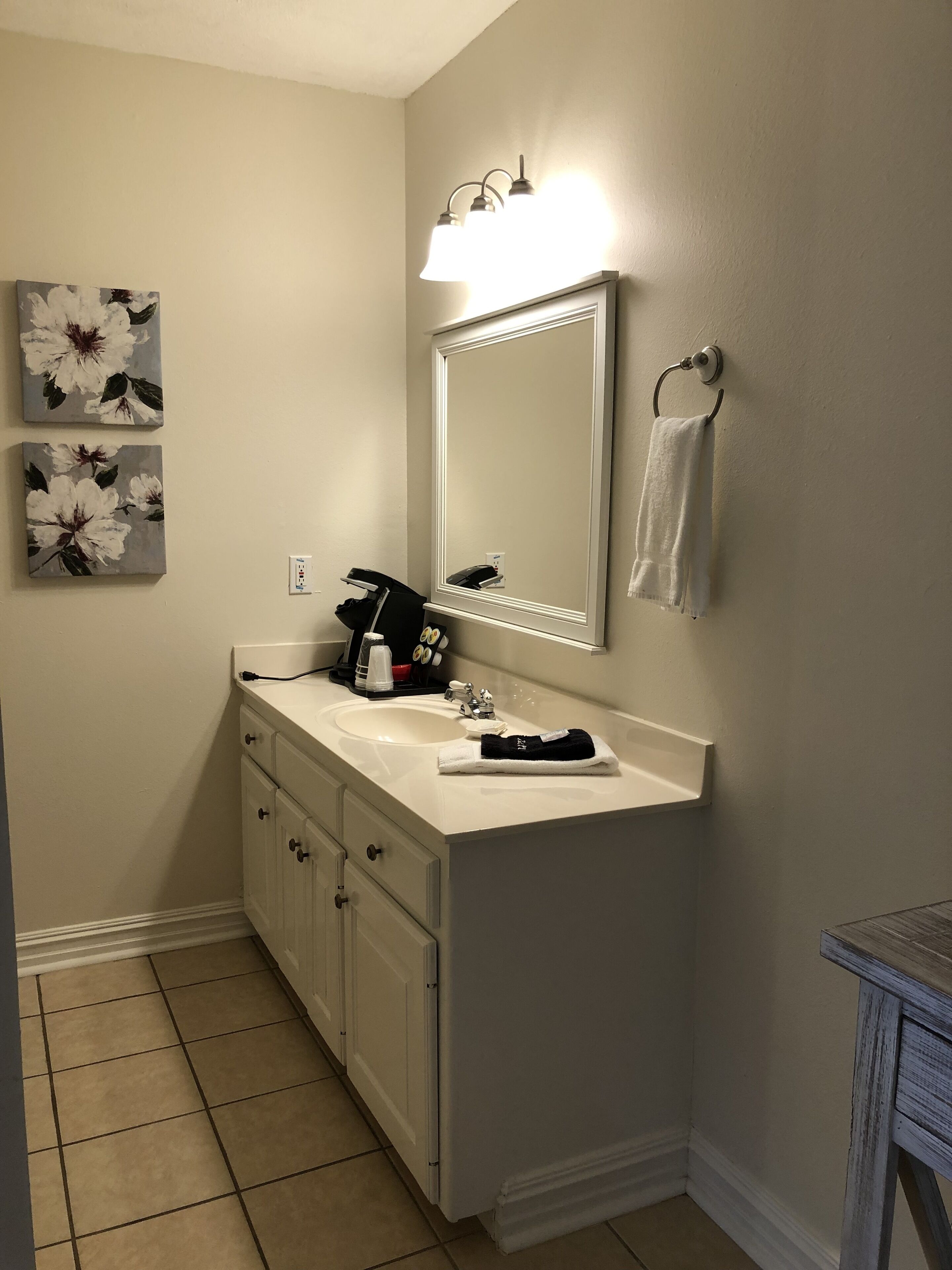 A bathroom with a white sink, a mirror, a towel rack, and two floral paintings on the wall.