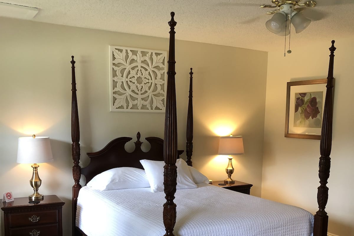 A four-poster bed with a wooden frame, two bedside tables with lamps, a decorative wall piece, and a patterned rug.
