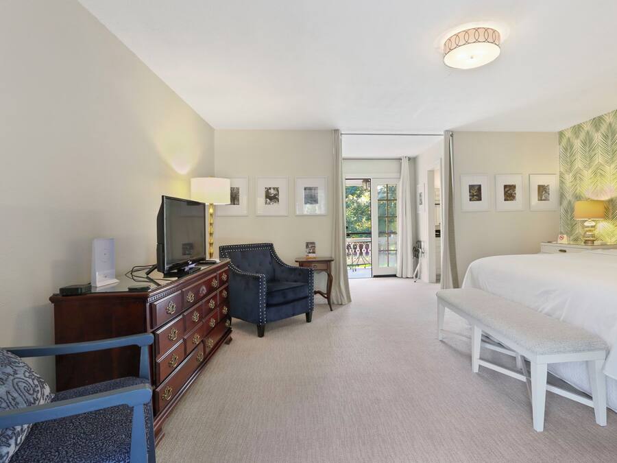 Ein Hotelzimmer mit einem großen Bett, einem Schreibtisch mit Computer, einem Sessel, einer Bank und einem Fernseher.