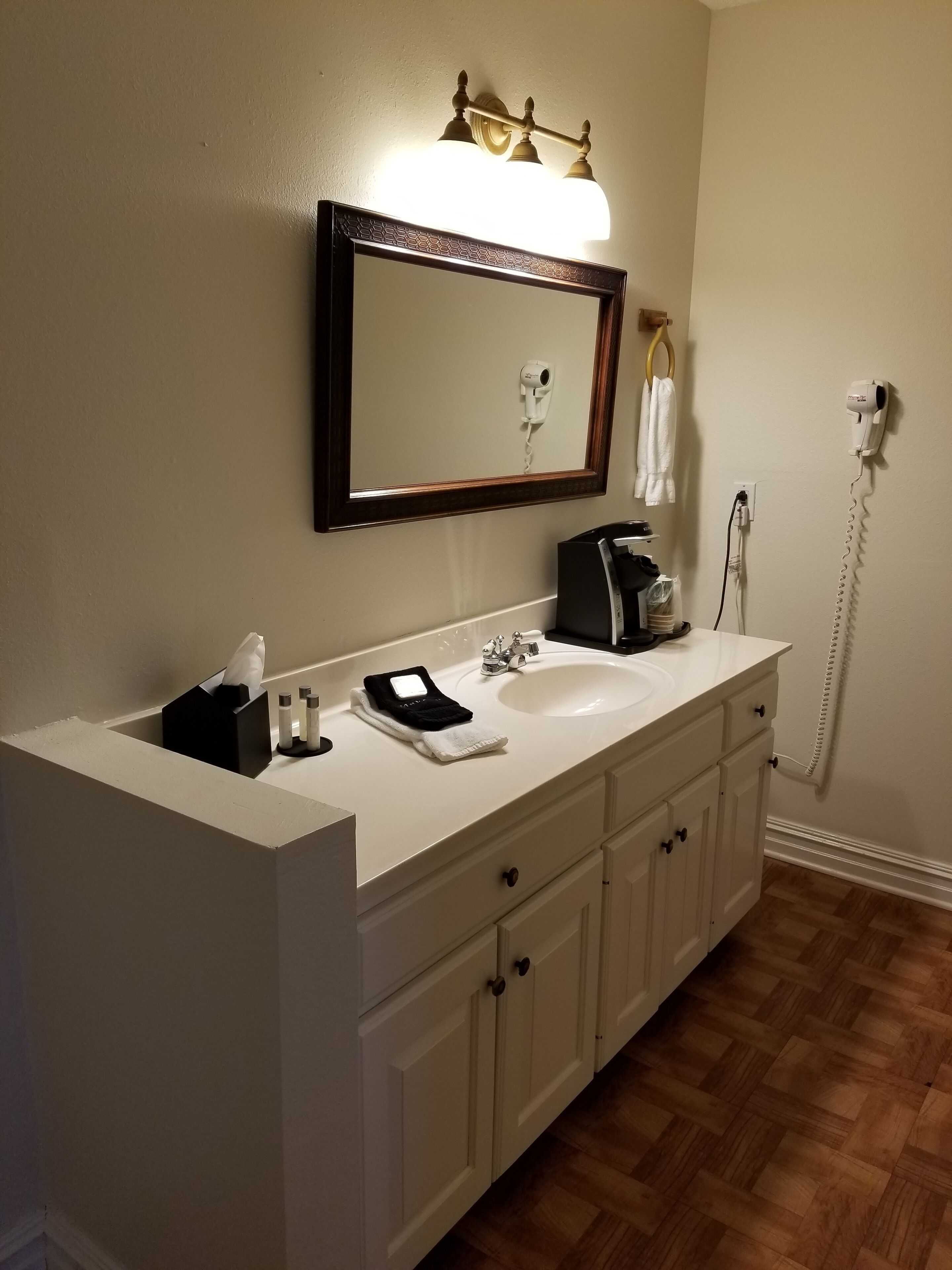 A bathroom with a white vanity, a mirror, a hairdryer, and a towel rack.