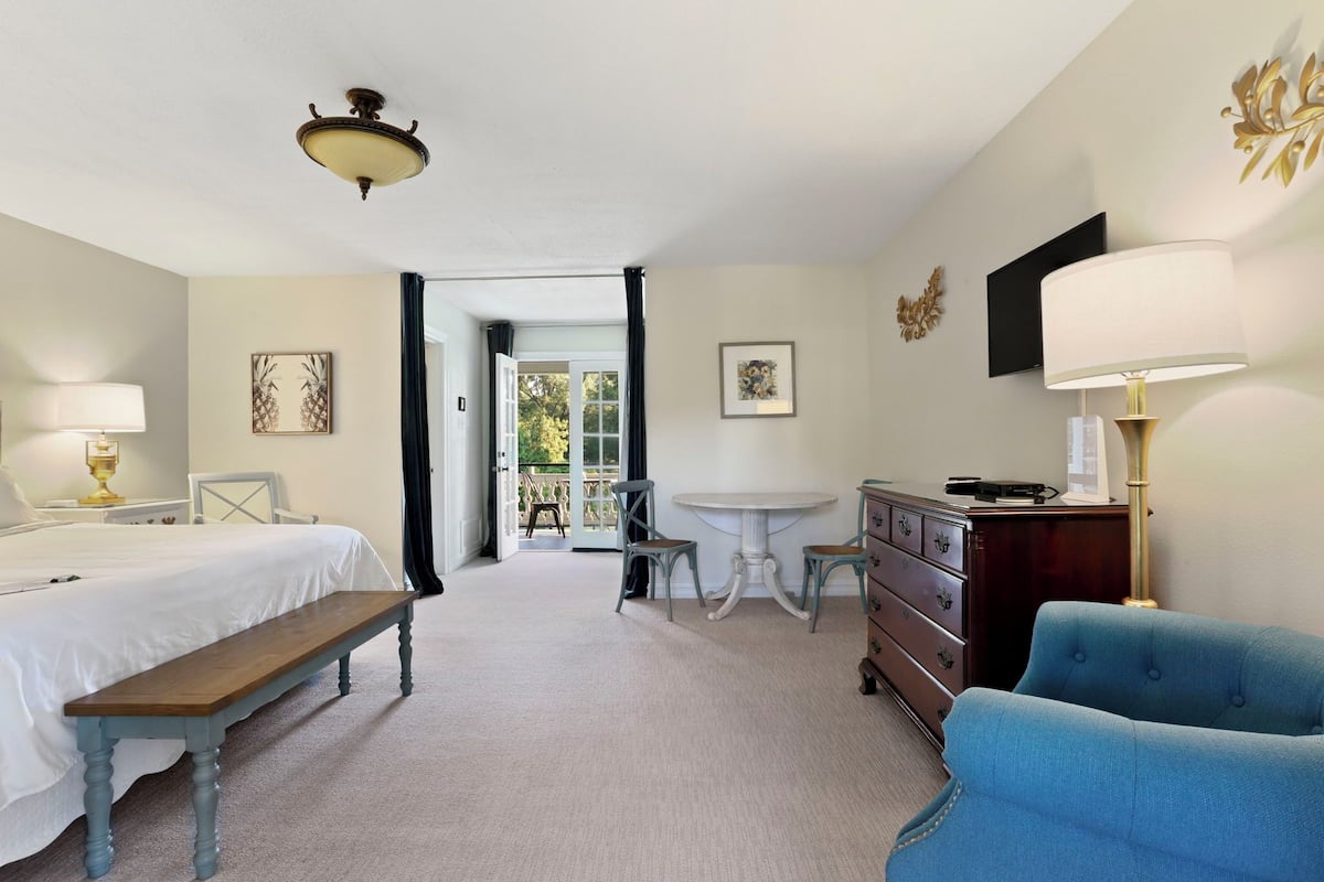 A hotel room with a bed, a bench, a dresser, a table with chairs, a lamp, and a ceiling fan.