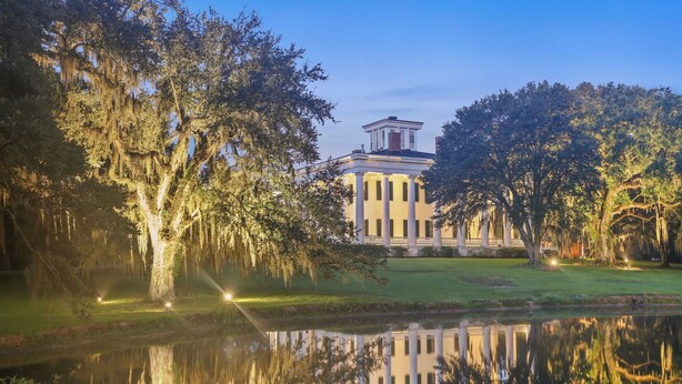 A stately building with a symmetrical facade, a central pediment, and a reflection in a calm body of water.