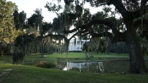 A large white building with a symmetrical facade, surrounded by a well-maintained lawn and a pond.