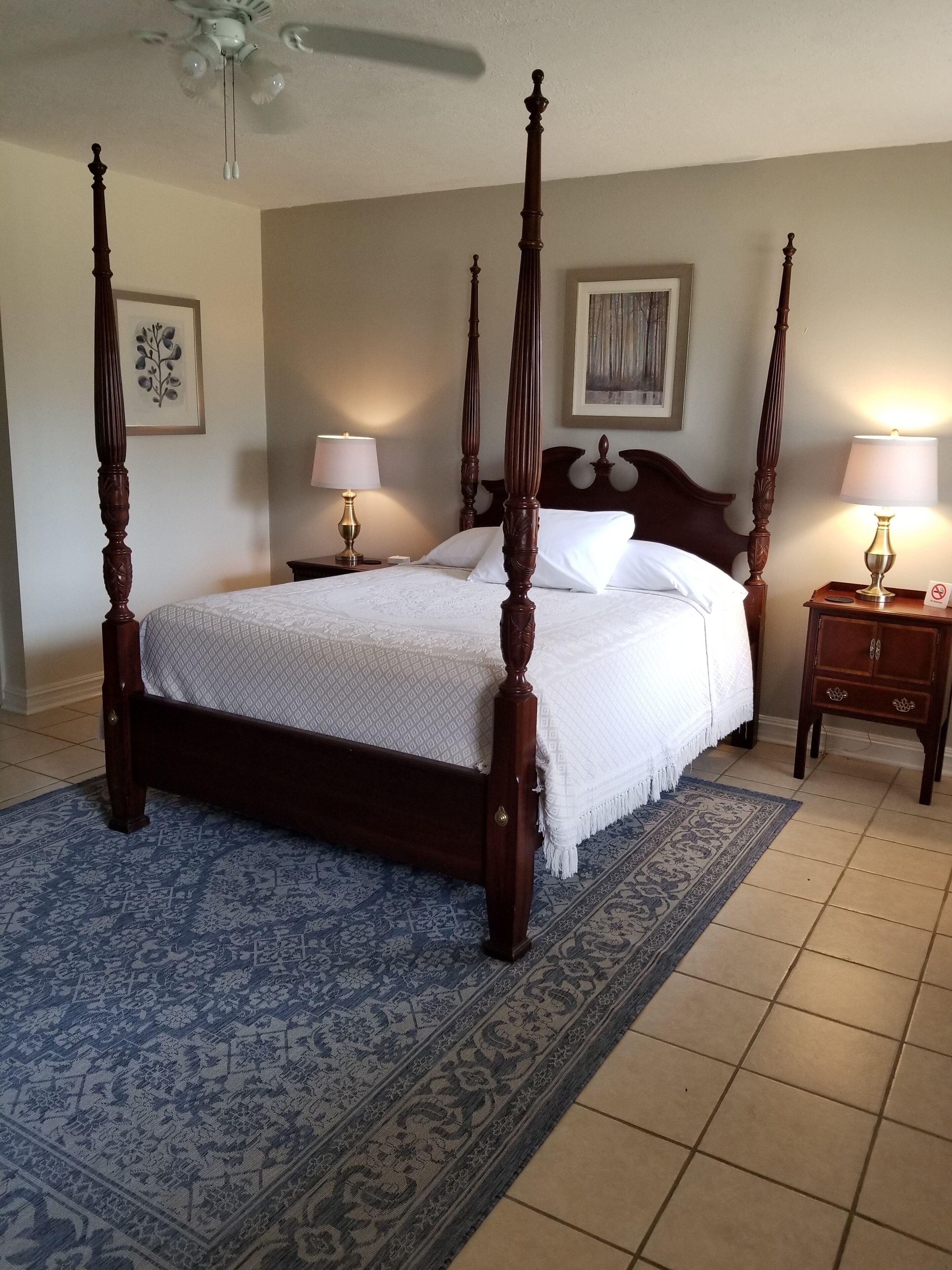 A four-poster bed with a white bedspread, two bedside tables with lamps, and a patterned rug.