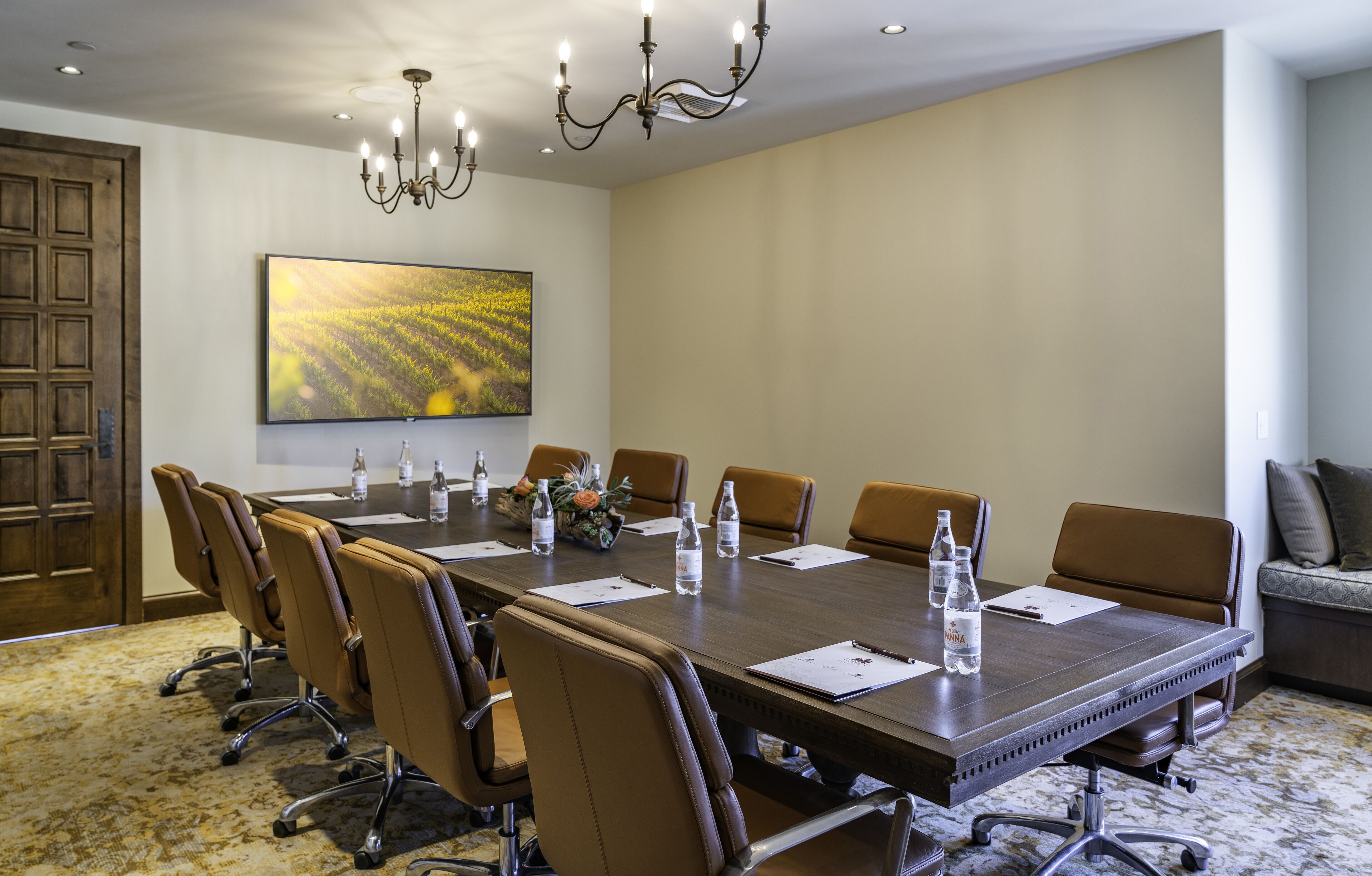A conference room with a long table, chairs, water bottles, and a chandelier.