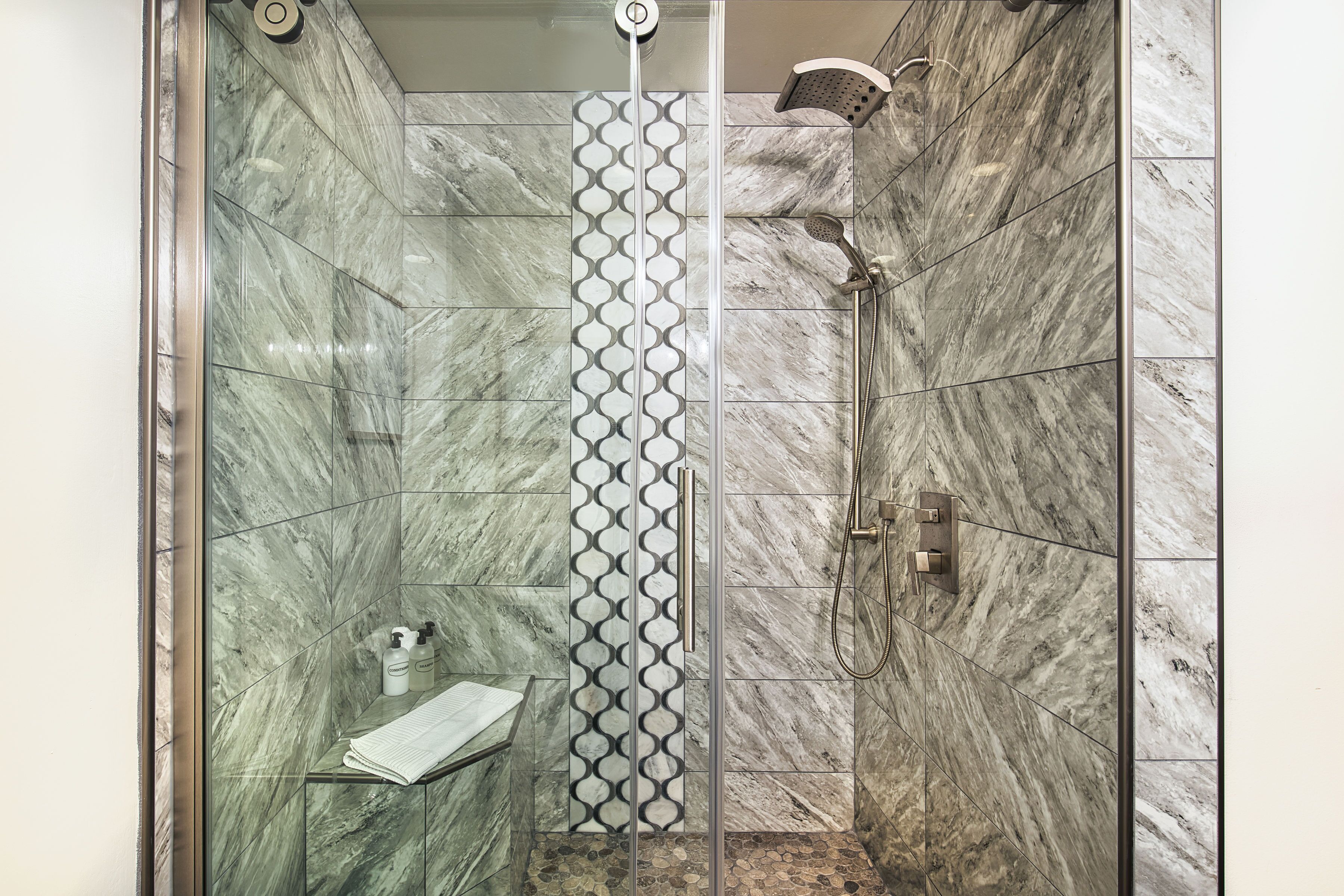 Un bagno moderno con doccia vetrata, parete rivestita di piastrelle decorate e pavimento in marmo.