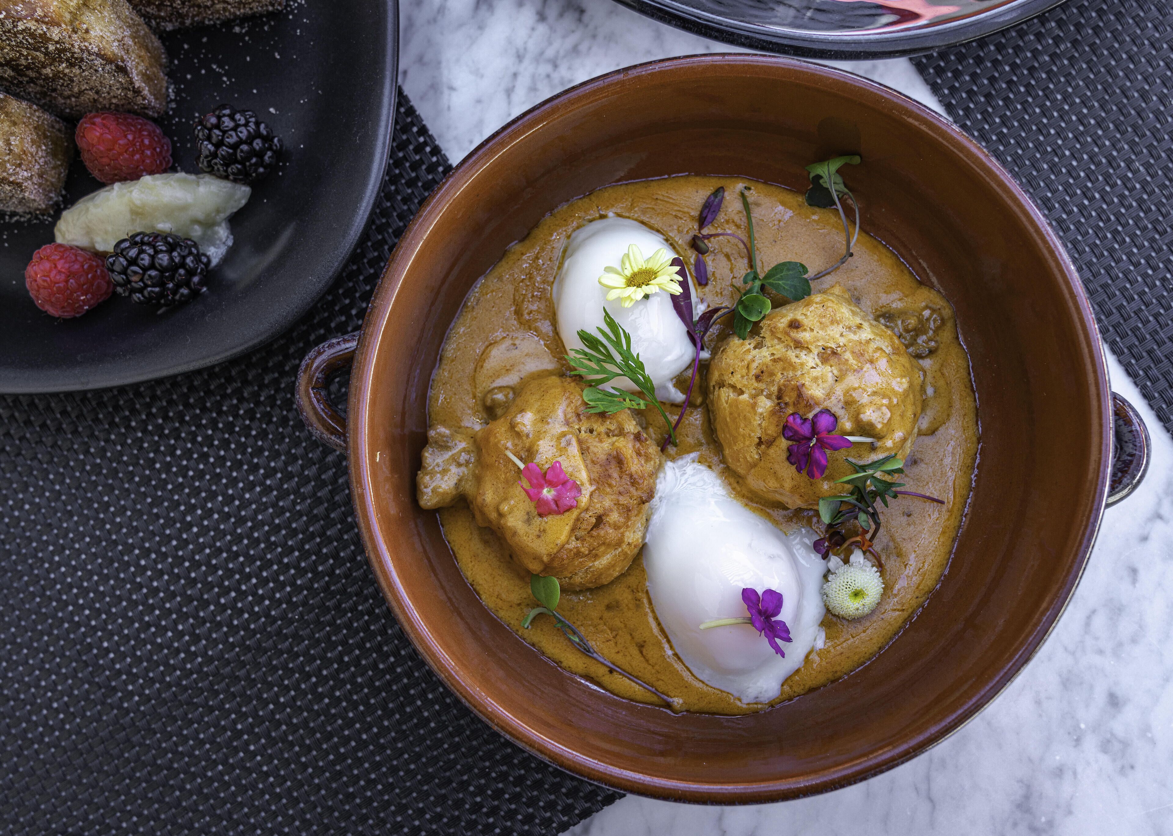 A bowl of curry with dumplings and garnishes, placed on a woven mat.