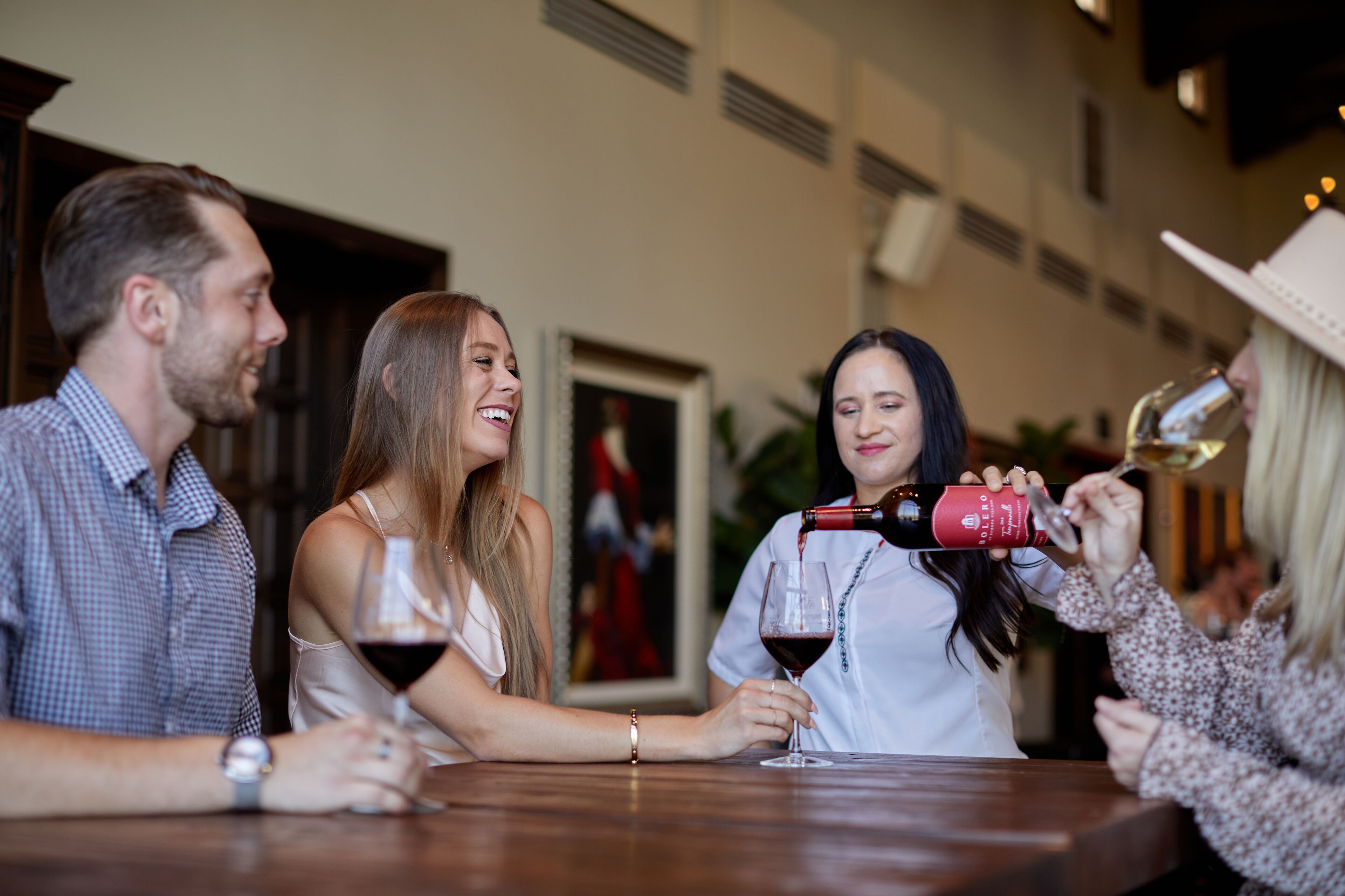 A group of people at a bar with wine glasses, a bottle of wine, and a bottle of champagne.
