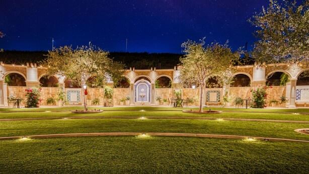 Un patio con una fuente central, rodeado de arcos y plantas en macetas, bajo un cielo estrellado.