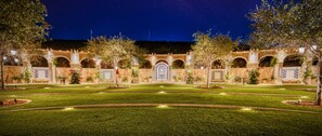 A courtyard with a central fountain, surrounded by arches and potted plants, under a starry night sky.