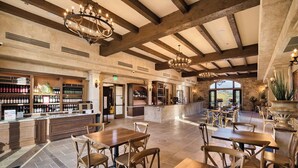 Amplia zona de bar con mesas y sillas de madera, una exhibición de vinos y vistas a través de amplios ventanales.