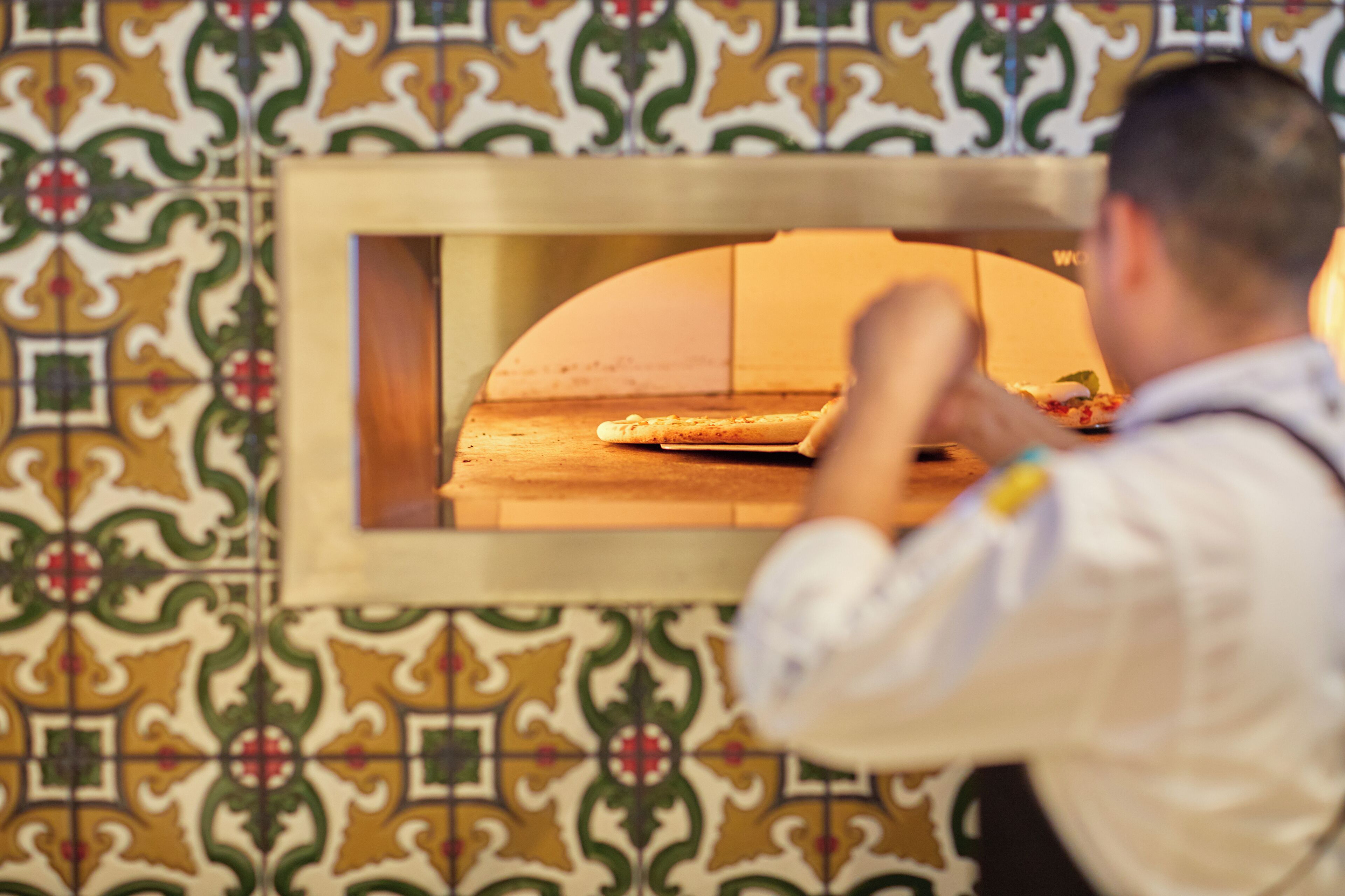 A person in a white shirt and apron working with a pizza in a brick oven.