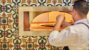 A person in a white shirt and apron working with a pizza in a brick oven.