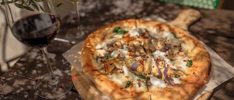 A pizza on a wooden board with a glass of red wine and a glass of white wine on the table.