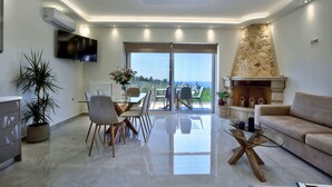 Un salon moderne avec une table basse en verre, un canapé, un coin repas avec des chaises, un téléviseur fixé au mur et une cheminée en pierre.