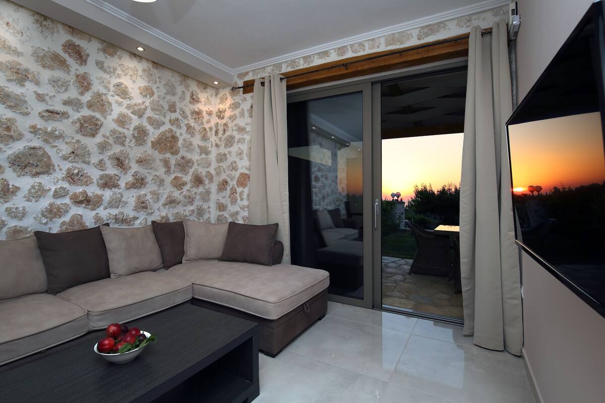 Una sala de estar moderna con un sofá seccional color beige, una mesa de centro oscura con un cuenco de fruta, y un televisor de pantalla plana grande.