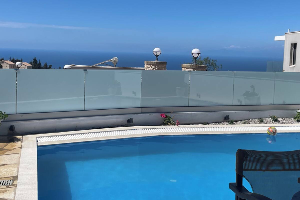 Una piscina con vista despejada al mar y una barandilla de vidrio.