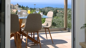 Un balcon avec une table et des chaises, offrant une vue panoramique sur la mer et la verdure.