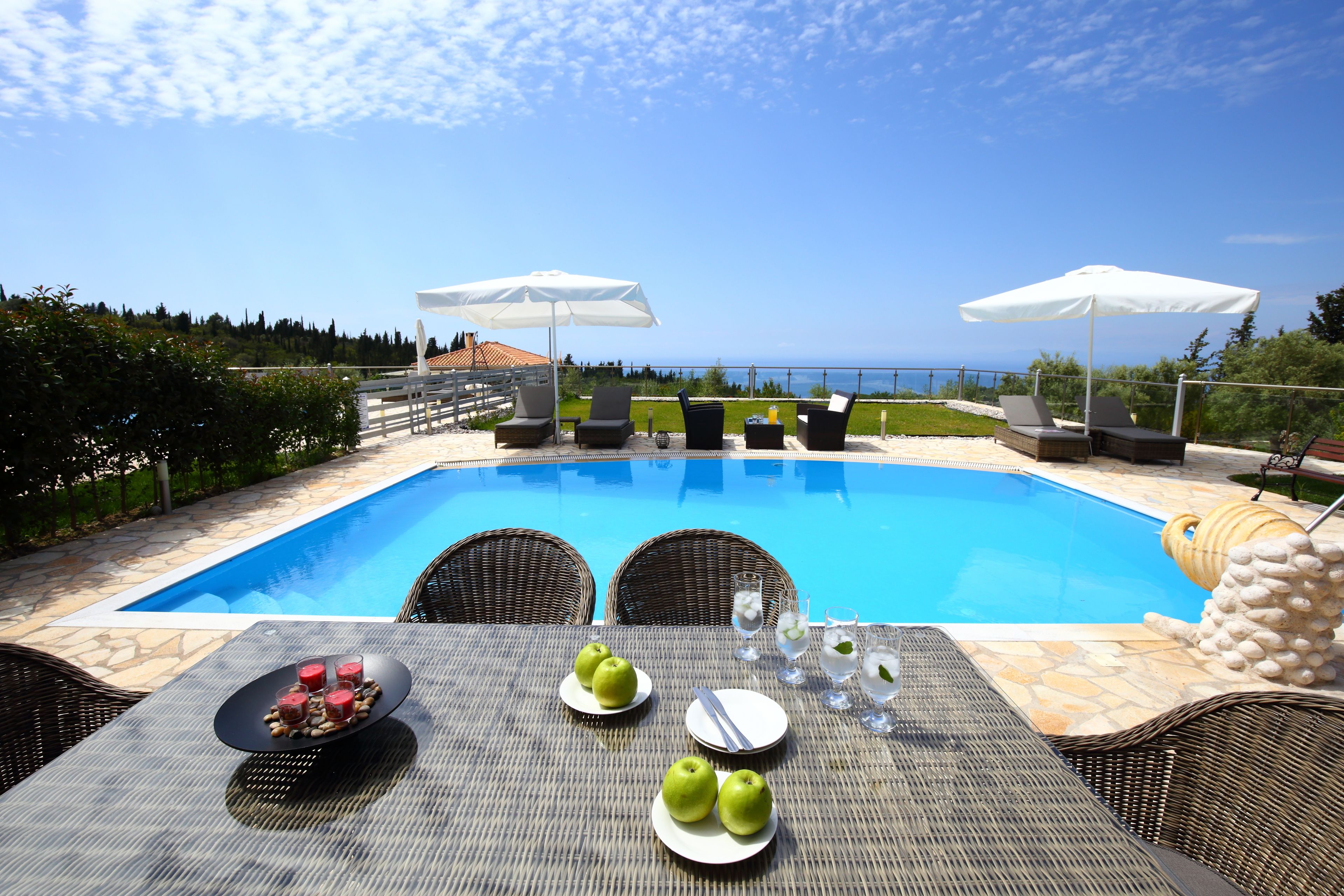 A poolside area with a table set for dining, outdoor chairs, and umbrellas.